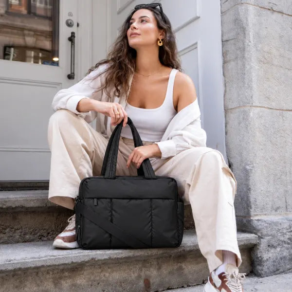 Illustrative woman in a white top with sunglasses on her head, seated on stone steps with the Black All-Day Tote