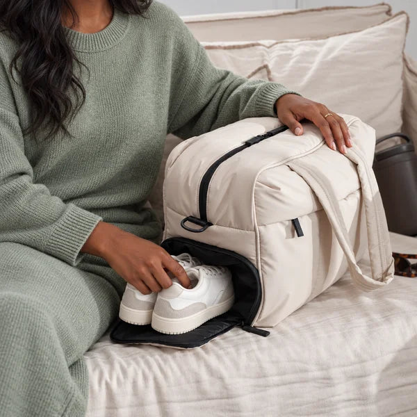 Illustrative image of a woman placing sneakers in the Cream All-Day Tote shoe compartment